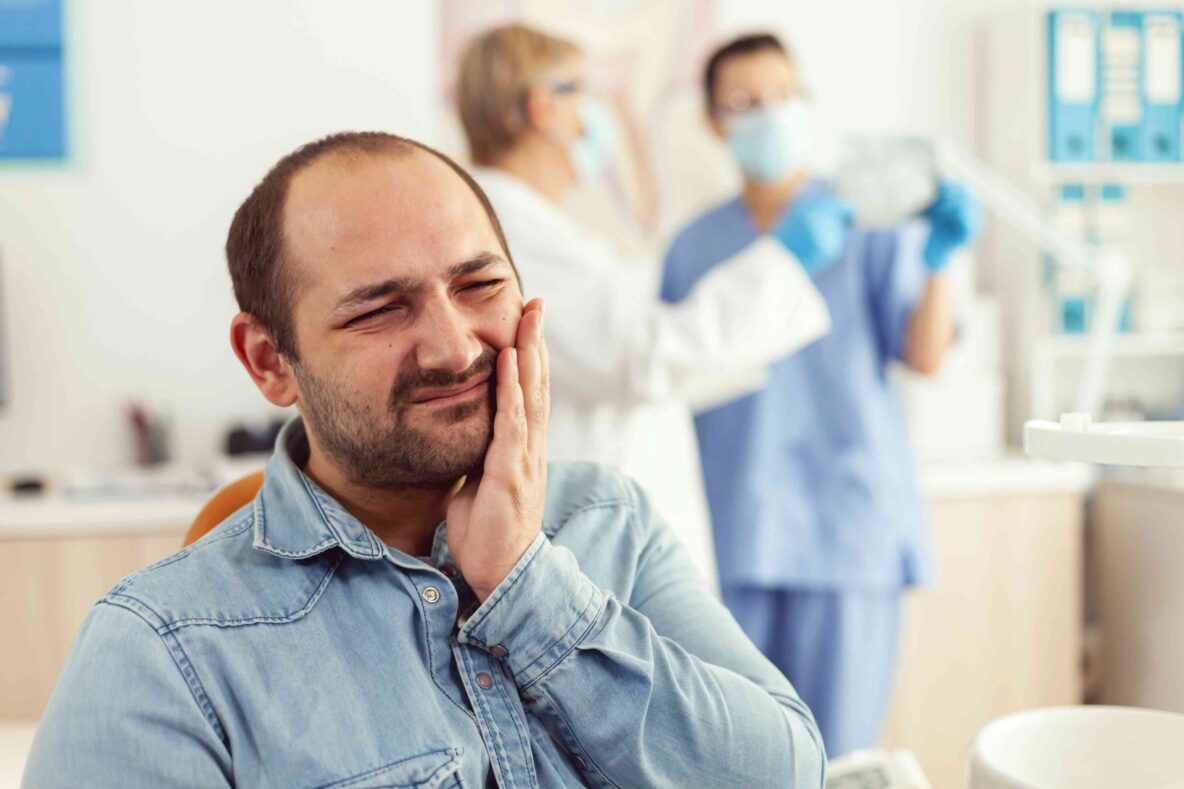 Man holding his jaw with a toothache in a dental office.